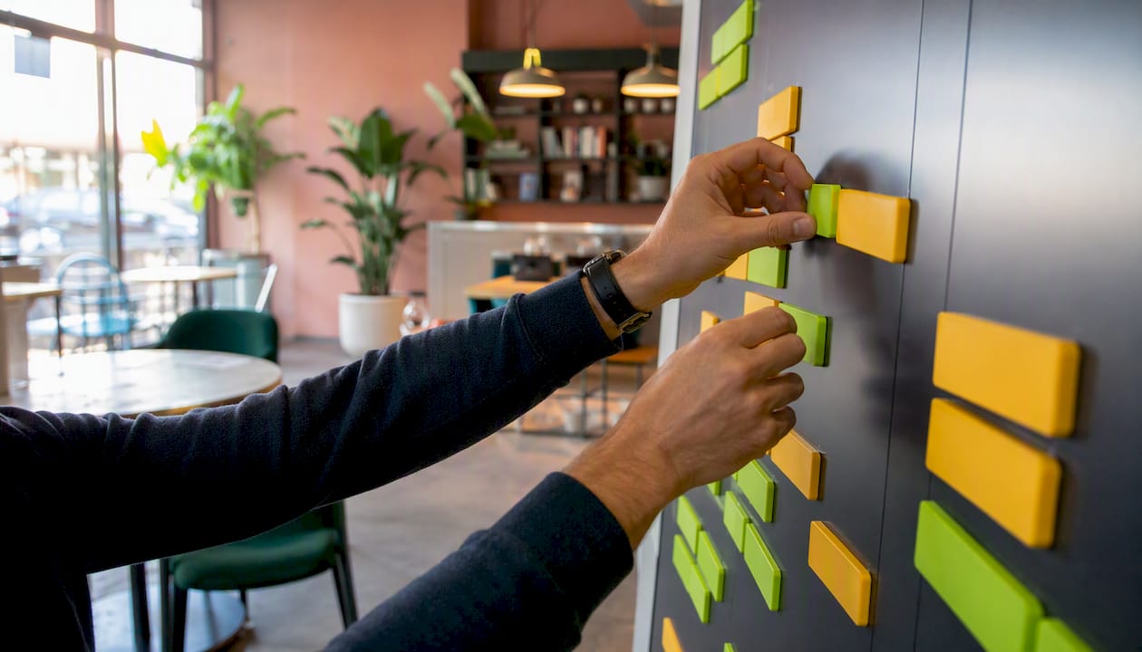Des mains disposent des blocs de planning sur un tableau magnétique, organisant ainsi l’emploi du temps de façon visuelle.