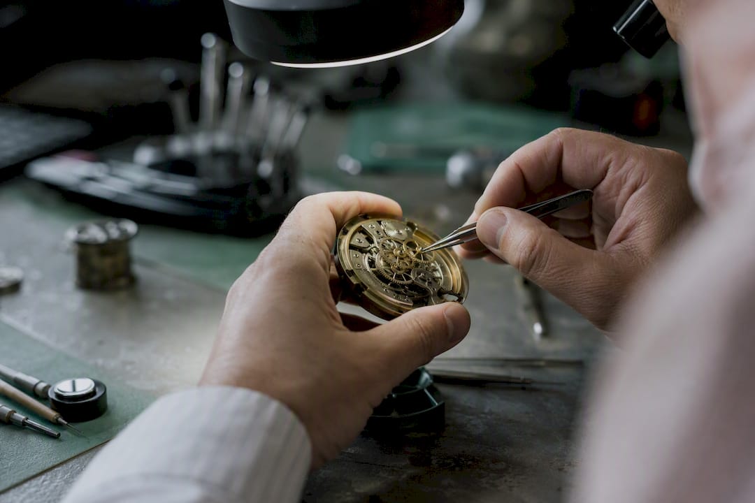 Des mains minutieuses règlent avec précision les rouages d’une horloge, capturées en gros plan.