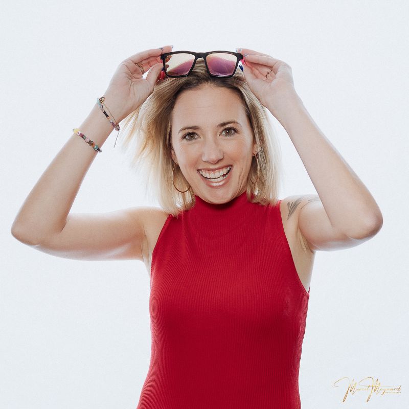 jeune femme blonde souriante portant un haut rouge et des lunettes de soleil relevées sur la tête